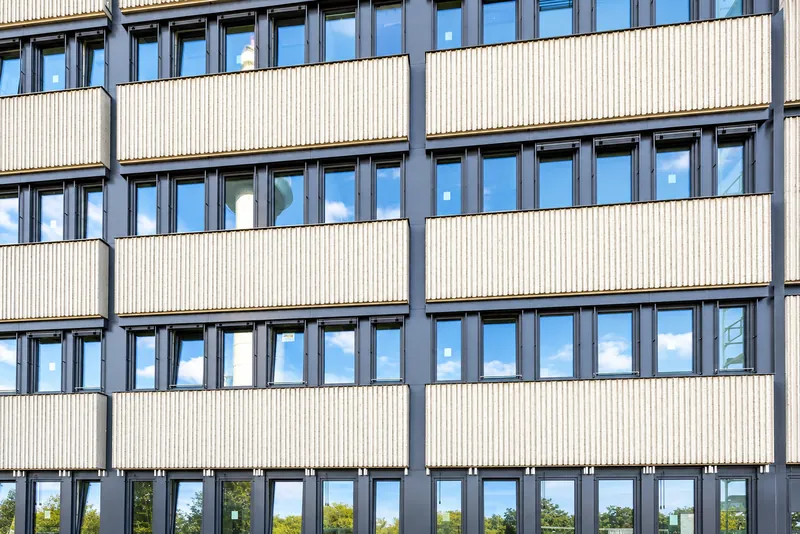 Gros plan de la façade : panneaux striés clairs et bandes de fenêtres gris ardoise