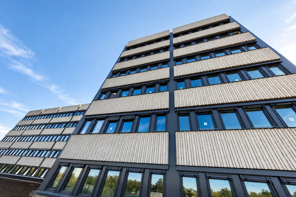 La façade rénovée vue d'en bas : panneaux striés en béton lavé clair et bandes de fenêtres gris ardoise